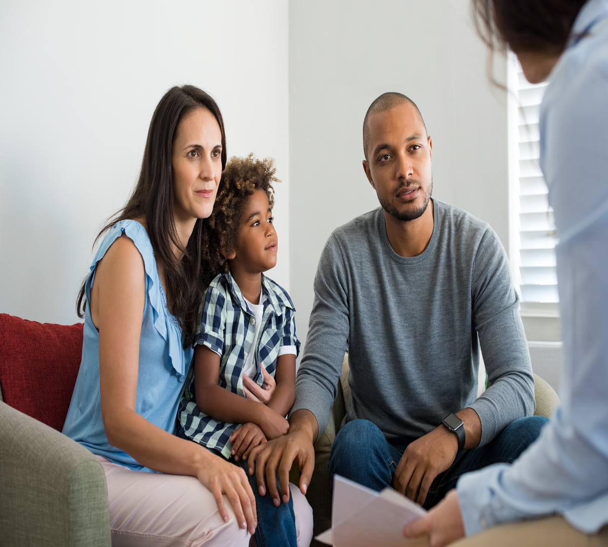 Serious couple with son in a deep conversation with family counselor. Multiethnic parents talking about adoption with their counselor. Family at the financial planning consultation.